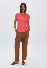 Koralli lyhythihainen t-paita, joka on yhdistetty ruskeisiin, väljiin pellavahousuihin. Asusteessa on pehmeitä tekstuureja ja rento siluetti.