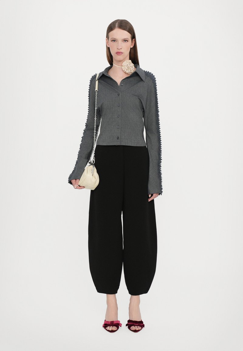 Grå skjorta med knäppning och texturerade ärmar, tillsammans med svarta vida byxor, en krämfärgad handväska och vinröda klacksandaler.