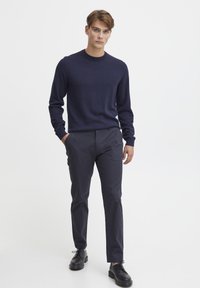 Marineblauer Pullover mit langen Ärmeln, kombiniert mit dunklen Hosen und schwarzen Schuhen. Einfaches Design, glatte Textur und taillierte Form.