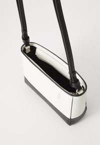 White and black compact handbag with leather material, rectangular shape, two black straps, and an interior zip pocket.