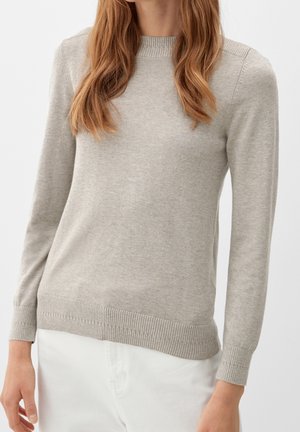 Woman wearing a light gray long-sleeve knit sweater with ribbed cuffs and hem, paired with white pants, against a plain background.