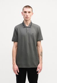 Tmavě šedé polo tričko s krátkým rukávem, s dvouknoflíkovou légou a pruhovaným límcem. Diskrétní logo na levé hrudi. Hladká textura.