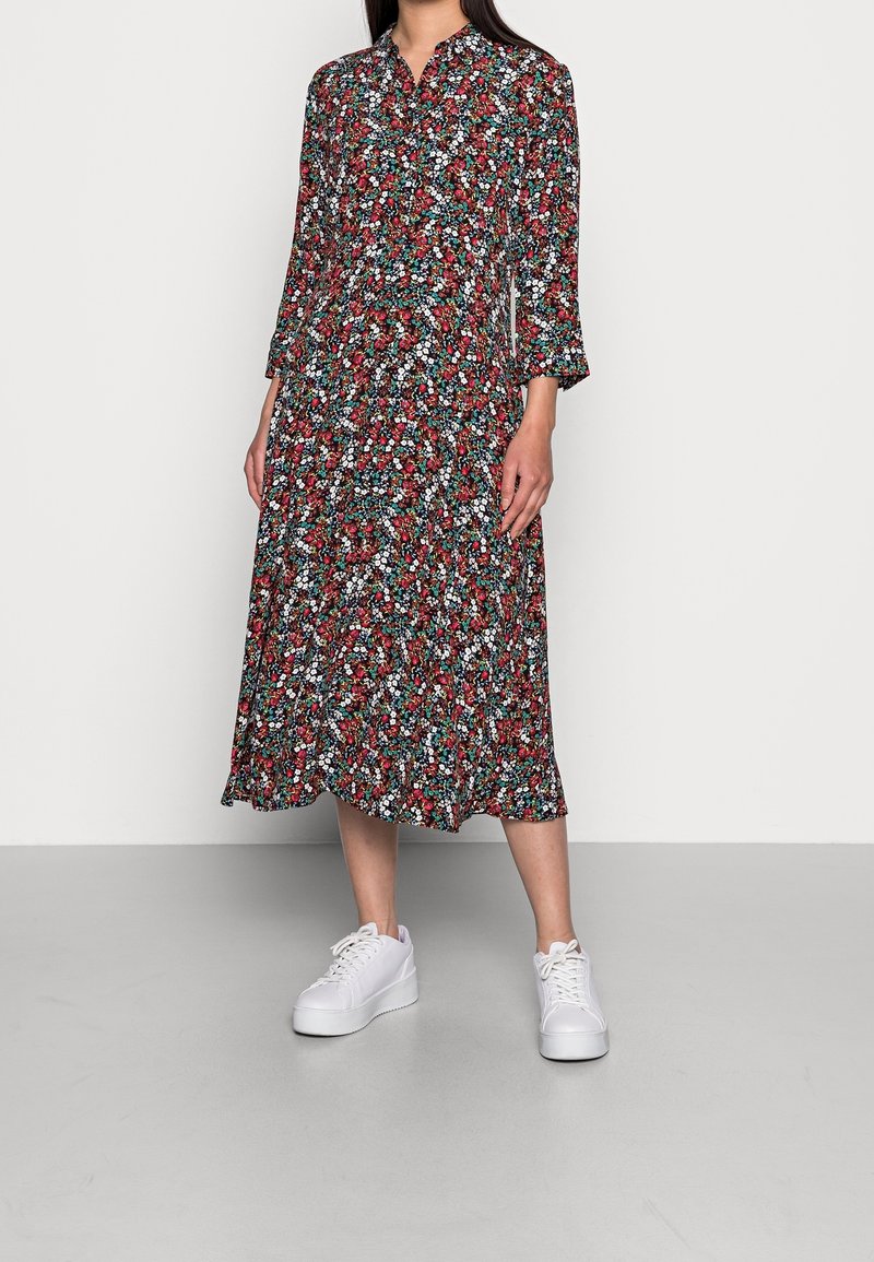 Robe midi fleurie avec des motifs rouges, blancs et verts, dotée d'un col chemise et de manches trois-quarts. Association avec des baskets blanches.