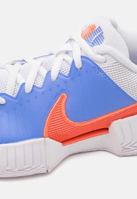 Blå og orange atletisk sko med en tekstureret overdel, mesh-paneler, hvide snørebånd og et fremtrædende orange logo. Gummisål.