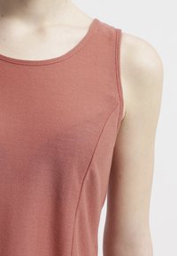 Top sin mangas color rosa, hecho de una tela texturizada, con escote redondo y costuras sutiles para un ajuste entallado.