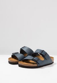Twee blauwe flip-flop sandalen met twee verstelbare banden, kurken voetbed en een gestructureerde zwarte rubberen buitenzool.