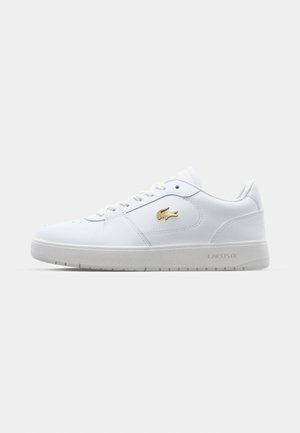 White sneakers made of leather, featuring a subtle gold logo, light gray sole, and round toe design. Laces and padded tongue included.