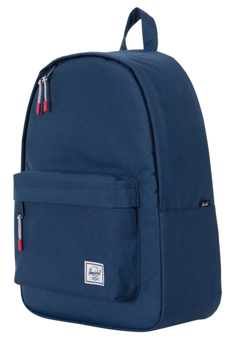 Sac à dos en tissu bleu marine à forme arrondie, avec une poche avant et des zips doubles avec des accents rouges. Équipé d'une poignée supérieure et d'une étiquette de marque.