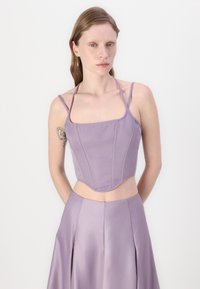 Lilla crop top med tynne stropper, strukturert liv med sømmer, og en buet hem. Den glatte satin teksturen komplementerer den matchende skjørtet.