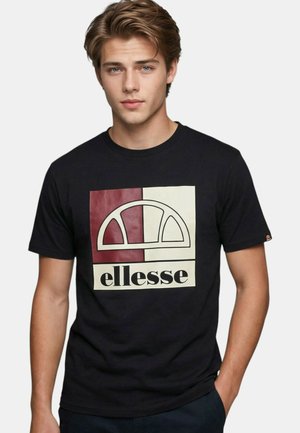 Jeune homme aux cheveux châtain clair portant un t-shirt noir avec un carré rouge et blanc et le logo "ellesse" sur la poitrine.