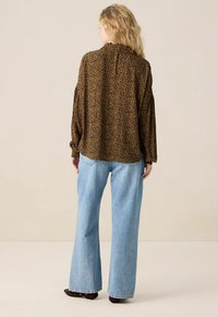 Blouse à manches longues, imprimé léopard marron avec une coupe décontractée, associée à un jean à jambes larges bleu clair, offrant une silhouette ample et un tissu doux.