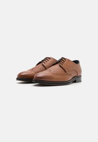 Chaussures habillées en cuir marron avec une finition lisse et des détails de brogue perforés. Présente une pointe arrondie et des lacets noirs.