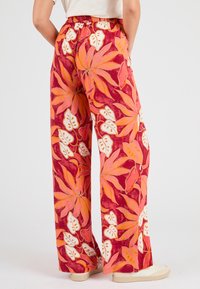 Pantaloni a gamba larga realizzati in un tessuto leggero e vivace che presenta grandi fantasie floreali in rosso, arancione e bianco su uno sfondo scuro.