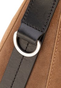 Attacco della tracolla della borsa in camoscio marrone e pelle nera con anello metallico argentato. Dettagli di cucitura visibili sulla pelle e sul camoscio.