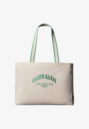 Beżowa torba typu tote z uchwytami obszytymi zielonym paskiem, z zielonym haftowanym napisem "Calvin Klein New York City" na przodzie.