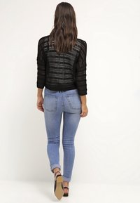 Jersey negro de punto con un corte holgado y mangas de tres cuartos, combinado con jeans skinny de color azul claro y sandalias de tacón negras.