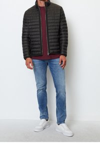 Sort puffjakke med vandrette kanaler, lynlås lukning, høj kind krave, båret over en bordeaux skjorte, parret med lyseblå jeans og hvide sneakers.