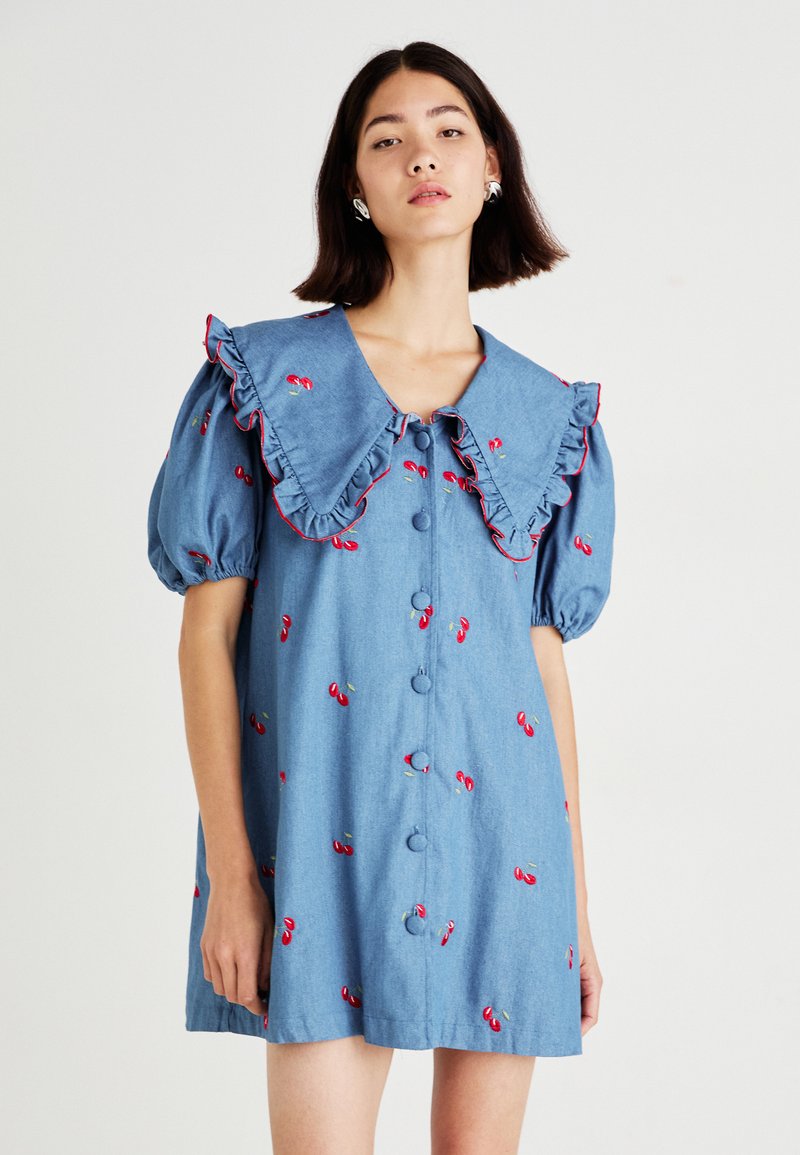 Světle modré denim šaty s velkým volánkovým límcem, krátkými nabíranými rukávy, knoflíky vpředu a červenými výšivkami třešní po celém povrchu.