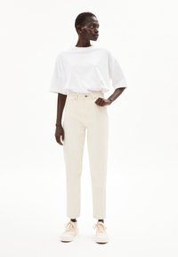 Vit oversized t-shirt i bomull, kombinerad med högmidjade beiga jeans i denim och lätta sneakers, med en rak skärning och minimala sömdetaljer.