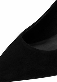 Scarpa con tacco alto in suede nero, con punta affilata, caratterizzata da un interno liscio e un design con scollo basso. Superficie testurizzata senza hardware visibile.