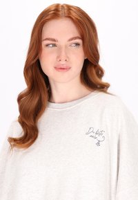 Světle šedý oversized svetr s kulatým výstřihem, zdobený modrým vyšitým textem "Du bist mein" a malým designem kotvy na hrudi.