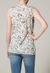 Top senza maniche con un motivo marmorizzato bianco e nero. Tessuto morbido, vestibilità rilassata con orlo arrotondato, abbinato a jeans blu chiaro.