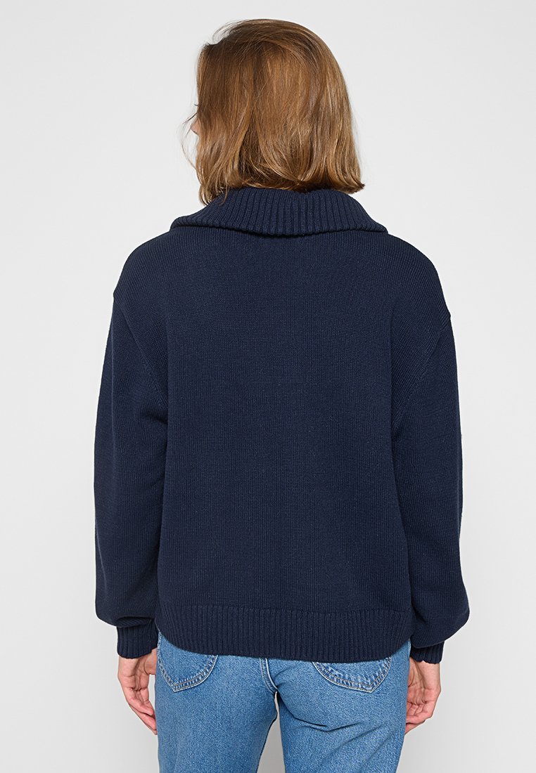 Jersey de punto azul marino con cuello ancho, hombros caídos y puños acanalados. Corte casual, tejido texturizado y diseño de color sólido.