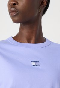 Svijetloplavi pamučni majica s kratkim rukavima, sa malom plavom i bijelom oznakom "TOMMY JEANS" na prsima, okruglim izrezom.