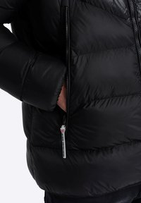 Schwarze Pufferjacke mit gestepptem Muster, seitlicher Reißverschlusstasche und hohem Kragen. Das Material ist glatt mit einem glänzenden Finish.