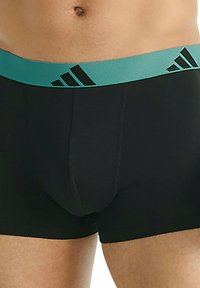 Svarta boxershorts med en teal-färgad elastisk midjeband som har tre svarta ränder. Materialet verkar slätt med minimala sömnadsdetaljer.