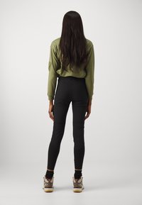 Olivgrön långärmad topp och svarta åtsittande leggings, med en slät yta. Bruna och krämfärgade sneakers med kontrasterande detaljer.