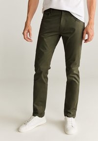 Olivgrön chinos i mjukt tyg med smal passform, framfickor och knäppt midja, kombinerat med vita sneakers.