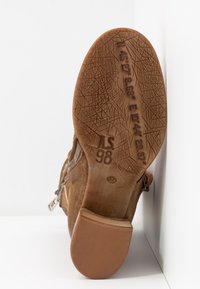Brown suede boot with a textured rubber sole, side zipper, and wooden heel accents. Features embossed details on the sole.