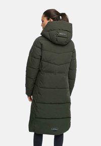 Manteau matelassé vert olive avec capuche, au design long, texture en chevrons, et logo de la marque près de l'ourlet.