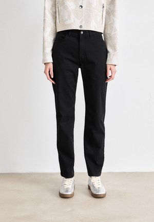 Black denim pants with a straight fit, featuring a button closure and five pockets, paired with light-colored sneakers.