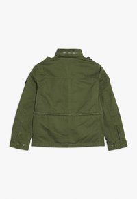 Oliwkowa kurtka o strukturalnym kroju, z guzikami przy mankietach i ściągnięciem w talii. Wykonana z trwałego materiału, posiada wentylację z tyłu oraz dyskretną kieszeń.