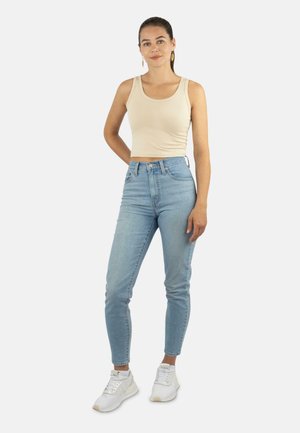 Beige-farbenes, enges Tanktop kombiniert mit hellblauen, hoch taillierten Jeans, getragen mit weißen Sport-Sneakern. Einfaches Design, glatte Textur.