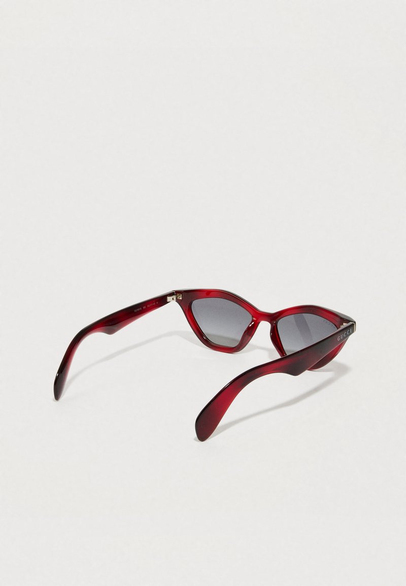 Rode plastic zonnebril met een cat-eye vorm, grijze lenzen en een glanzende afwerking. Heeft een logo-accent op de slaap.
