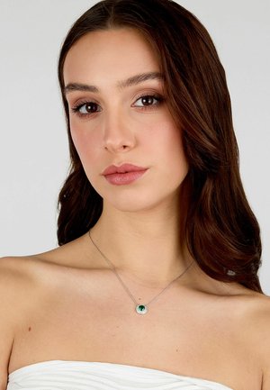 Collana d'argento con un pendente circolare caratterizzato da una pietra verde, incastonata in una cornice texture, indossata su una spalla nuda.