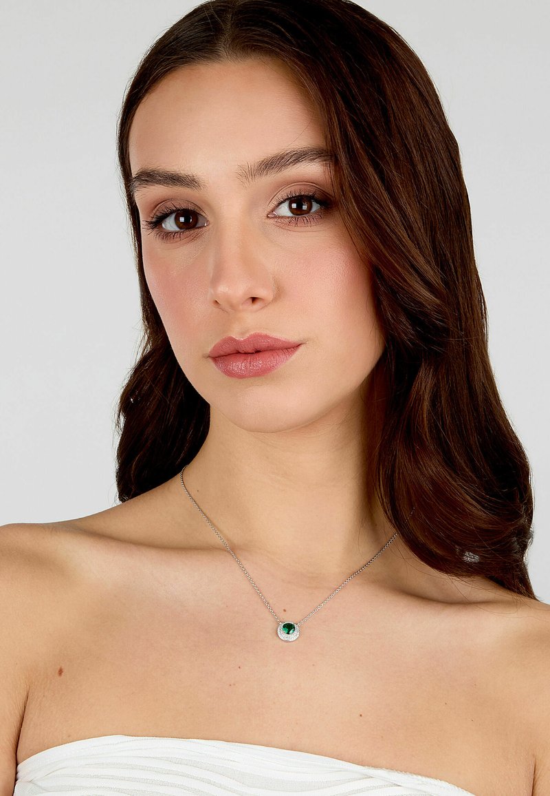 Collana d'argento con un pendente circolare caratterizzato da una pietra verde, incastonata in una cornice texture, indossata su una spalla nuda.