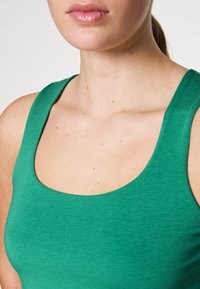 Camiseta sin mangas verde hecha de tela texturizada, con escote redondo y tirantes anchos, que muestra una silueta ajustada.