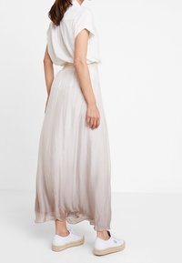 Maxi rok van transparant, lichtbeige materiaal, met een geplooide elastische tailleband. Gecombineerd met witte sneakers voor een casual uitstraling.
