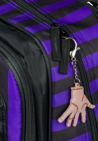 Zaino nero con strisce viola, dotato di un tirazip testurizzato. Da zip pende un portachiavi a forma di mano rosa con dettagli cuciti.