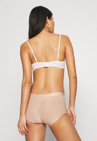 Bralet cu dungi roz deschis, cu bretele ajustabile și închidere cu cârlig, asociat cu lenjerie nude fără cusături. Textură netedă și design minimalist.