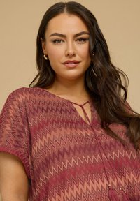 Blusa color marrone con motivo zigzag, tessuto leggero, scollo a V, maniche corte e dettaglio con nappina al centro davanti.