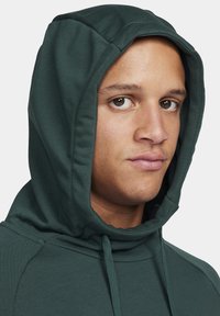 Dark green hooded sweatshirt made of ribbed fabric; features a drawstring hood and a close-up view of the face, showcasing brown eyes.