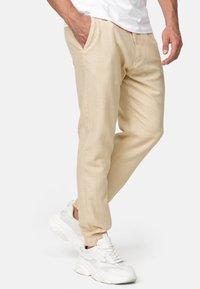 Pantalones jogger beige hechos de un tejido texturizado, con bolsillos laterales, puños elásticos y un ajuste entallado, combinados con zapatillas blancas.