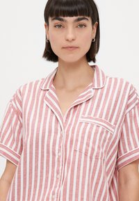 Chemise à manches courtes rayée rouge et blanche avec un devant à boutons, un col et une poche. Fabriquée en coton léger.