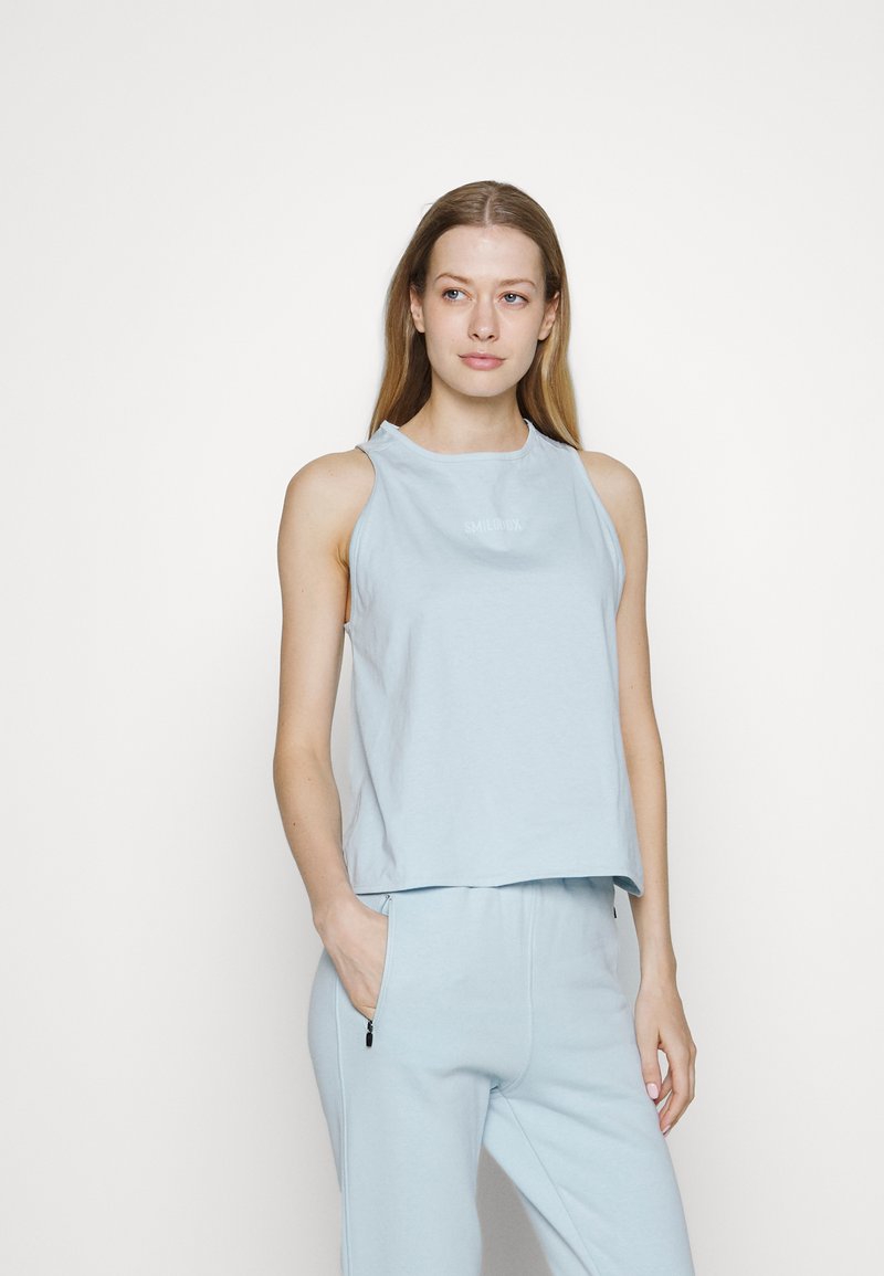 Top sem mangas azul claro em algodão macio com um corte descontraído. Apresenta um decote redondo e um pequeno logótipo "SMILUX" na parte da frente.