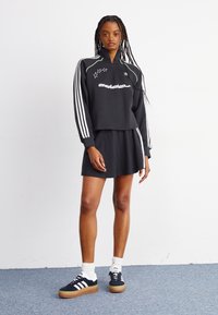 Czarna krótka bluza z białymi i zielonymi akcentami, z motywami gwiazd, zestawiona z dopasowaną czarną spódnicą i czarnymi trampkami.